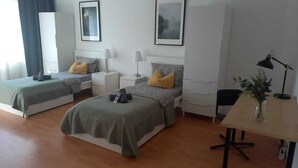 Una habitación de hotel moderna con dos camas individuales, un escritorio, una silla y una mesita de noche con un jarrón de flores.