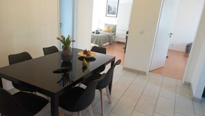 Un comedor moderno con una mesa y sillas negras, un jarrón con flores y un plato con fruta.