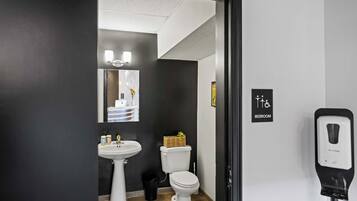 Casa de banho moderna com lavatório, sanita e dispensador de gel desinfetante, tudo em branco.