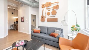 Ett modernt vardagsrum med en grå soffa, en orange fåtölj och ett soffbord. På väggen hänger en tavla med musikinstrument och på ett sidobord står en vas med blommor.