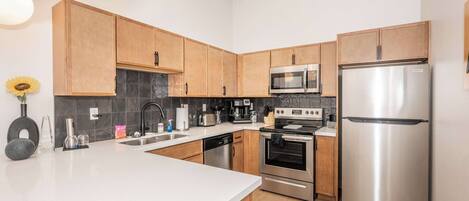 A modern kitchen with wooden cabinets, stainless steel appliances, and a white countertop.