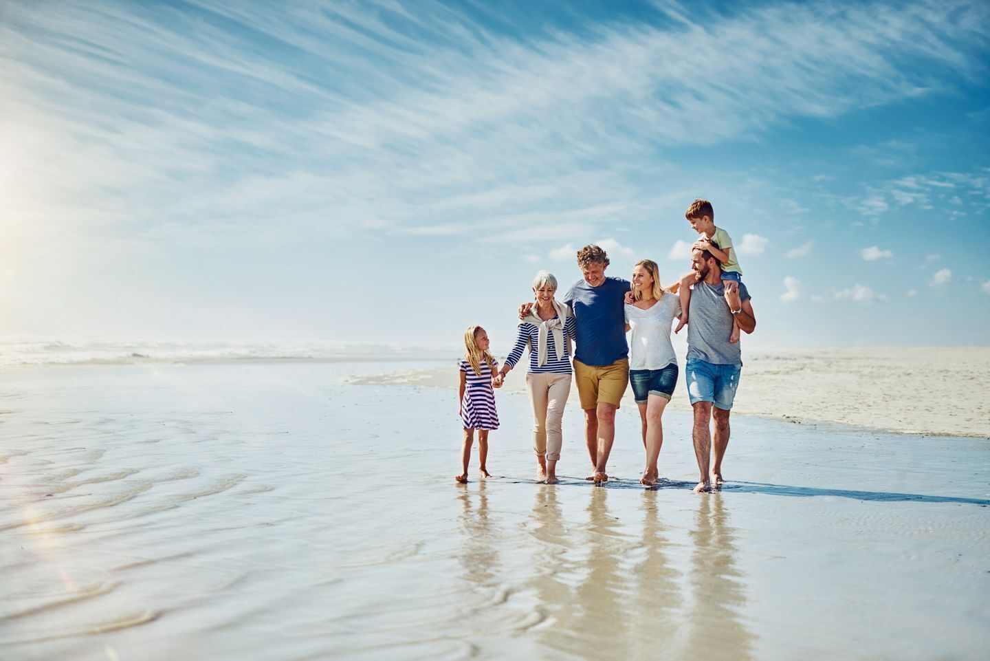 A family walking on a sandy beach with a clear sky.