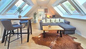 A loft-style living room with a high ceiling, skylights, a sofa set, a dining table, and a cowhide rug. - Apartment Turmblick - Comfortable apartment in the center of Marienhafe with (Marienhafe)