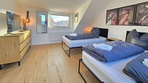 Un dormitorio tipo loft moderno con dos camas, un televisor, una guitarra y una ventana con vista a la ciudad.