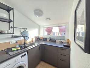 Eine kleine Küche mit einer Bosch Waschmaschine, einer Kaffeemaschine und einem Fenster mit Blick auf ein Gebäude mit rotem Dach.