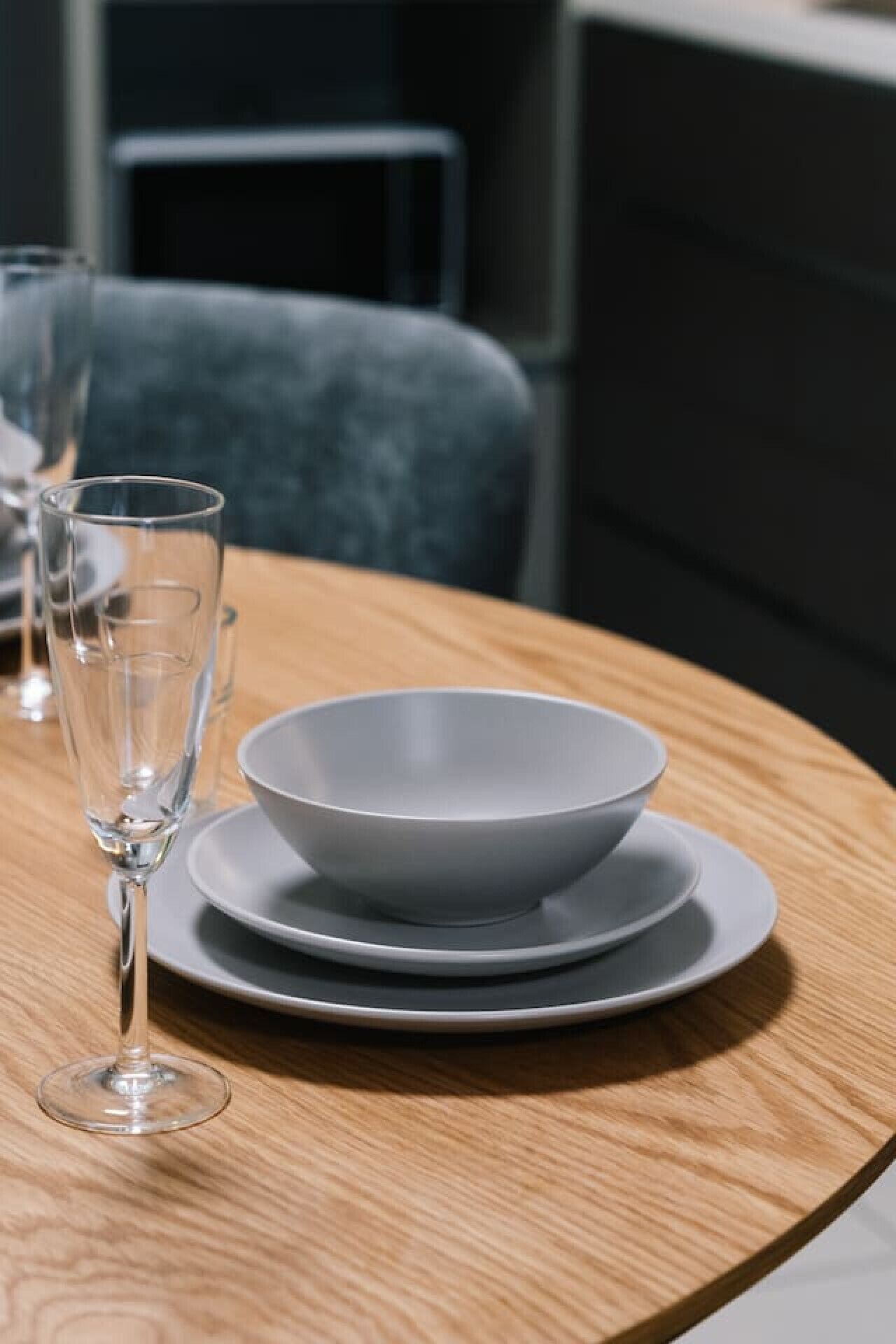 Een eettafel met een witte schaal en borden, een wijnglas en een stoel op de achtergrond.