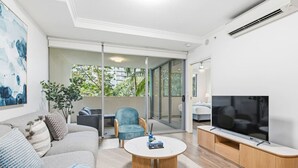 Een moderne woonkamer met een bank, fauteuil, salontafel, televisie en een schuifdeur naar een balkon.