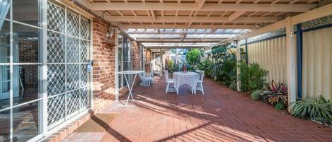 A covered patio with a brick floor, white outdoor furniture, and a glass door on the left.