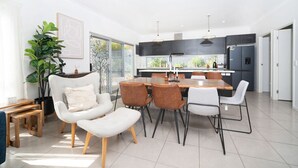 Un salon moderne comprenant un canapé, des fauteuils et une table à manger. Il y a également un coin cuisine avec des placards et un réfrigérateur.