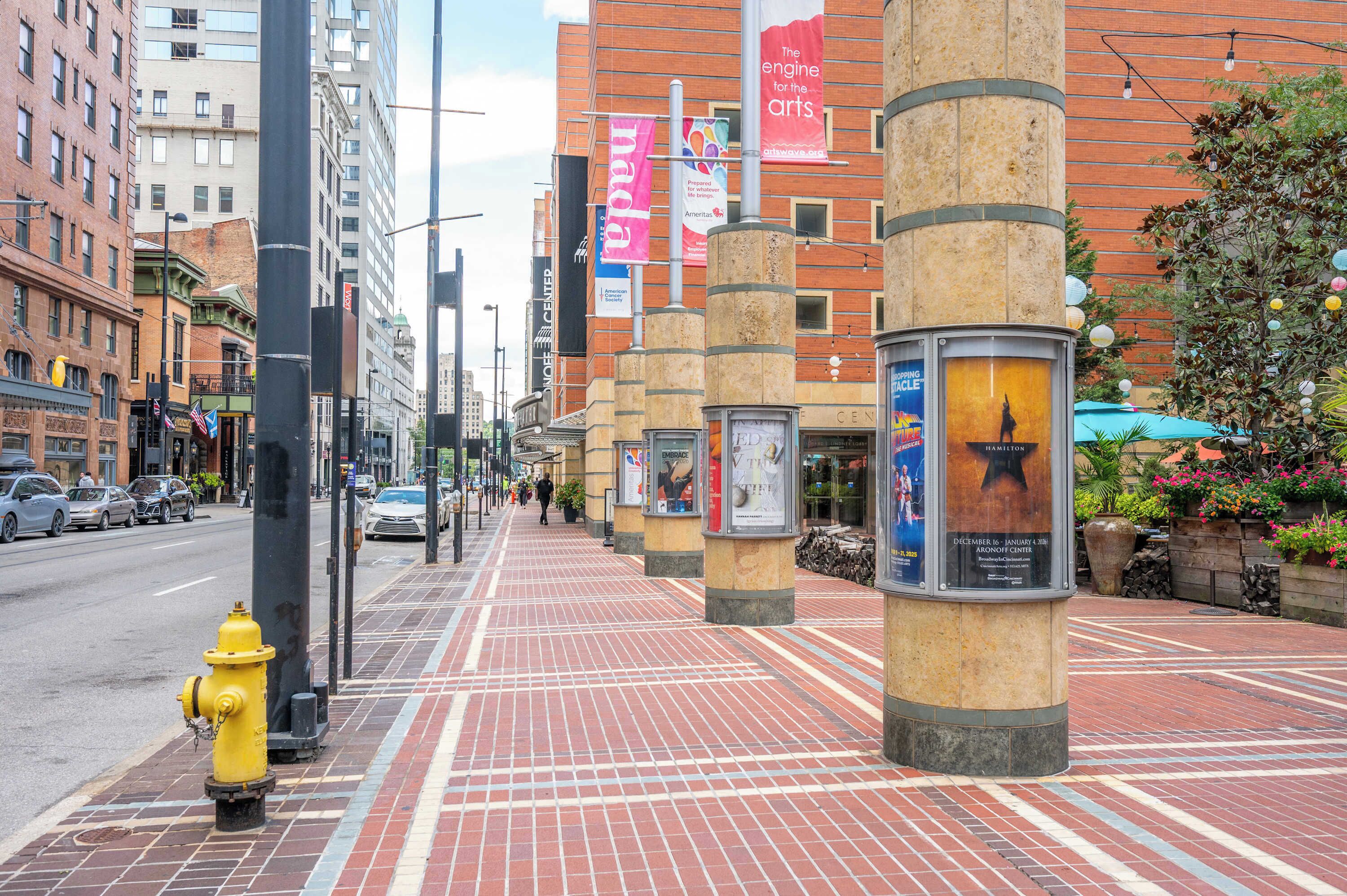 A city street with a yellow fire hydrant, brick sidewalks, and tall buildings with various banners.