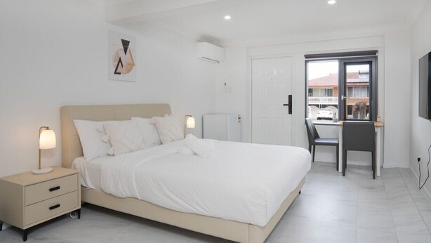 A bedroom with a bed, bedside tables, a desk, and a chair. - Modern 1BR Apartment | Convenient Stay (MacGregor)