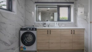 A modern bathroom with a built-in washing machine, a large mirror, and a wooden vanity with cabinets. - Modern Private Retreat | Perfect for Solo Traveler (MacGregor)