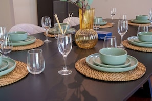 Mesa de comedor dispuesta con varios platos, tazones y copas de vino, junto a un jarrón decorativo y palillos.