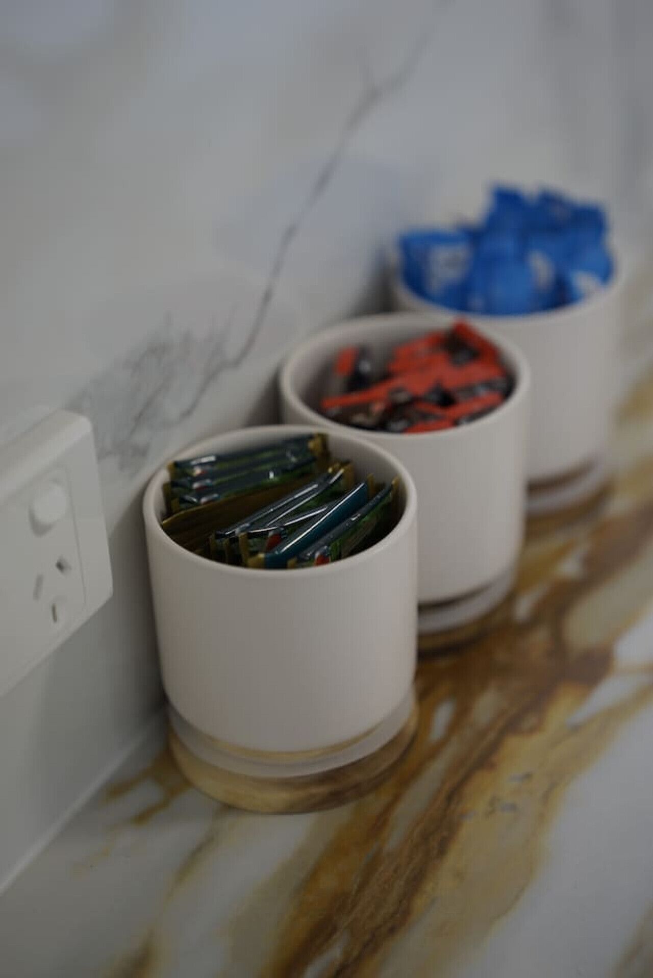 Two white cylindrical containers with colorful objects inside, placed on a marble surface near a white wall with a power outlet.