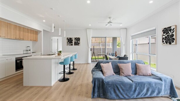 A modern kitchen with white cabinets, a central island with bar stools, and a dining area with a table and chairs.