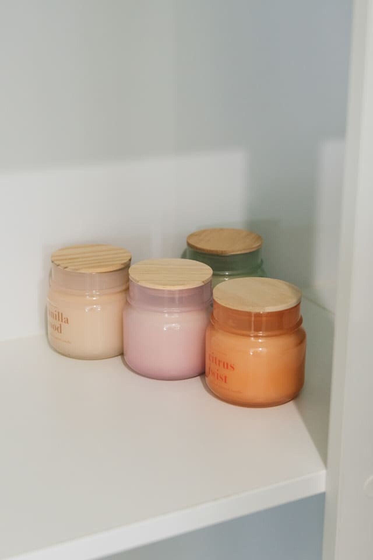 Four jars with different colored lids on a white shelf.