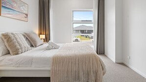A hotel room with a bed, a window with curtains, a painting on the wall, and a view of the outside.