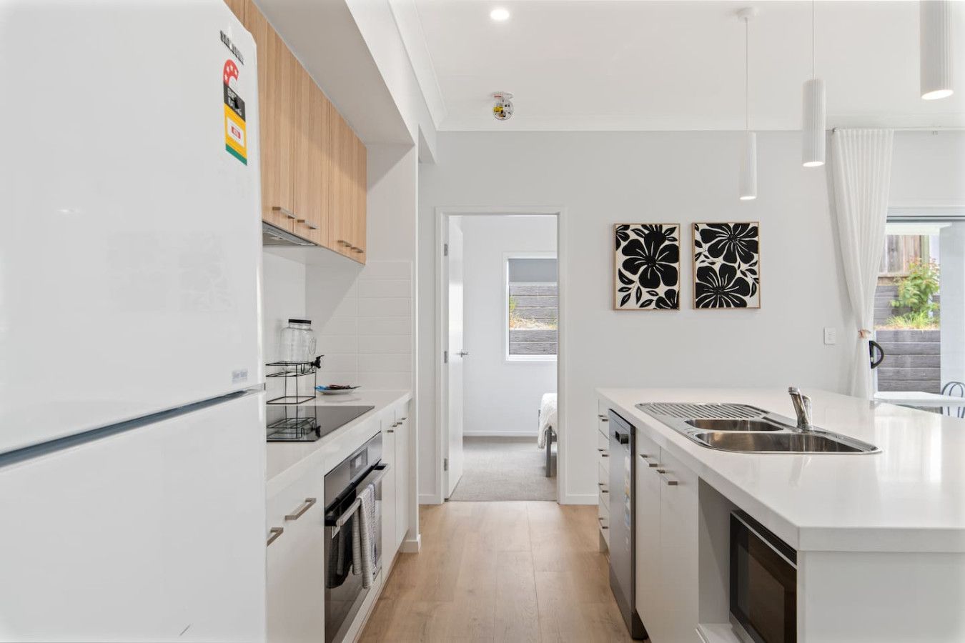 A modern kitchen with white cabinetry, a built-in oven, a stainless steel sink, and a window providing natural light.