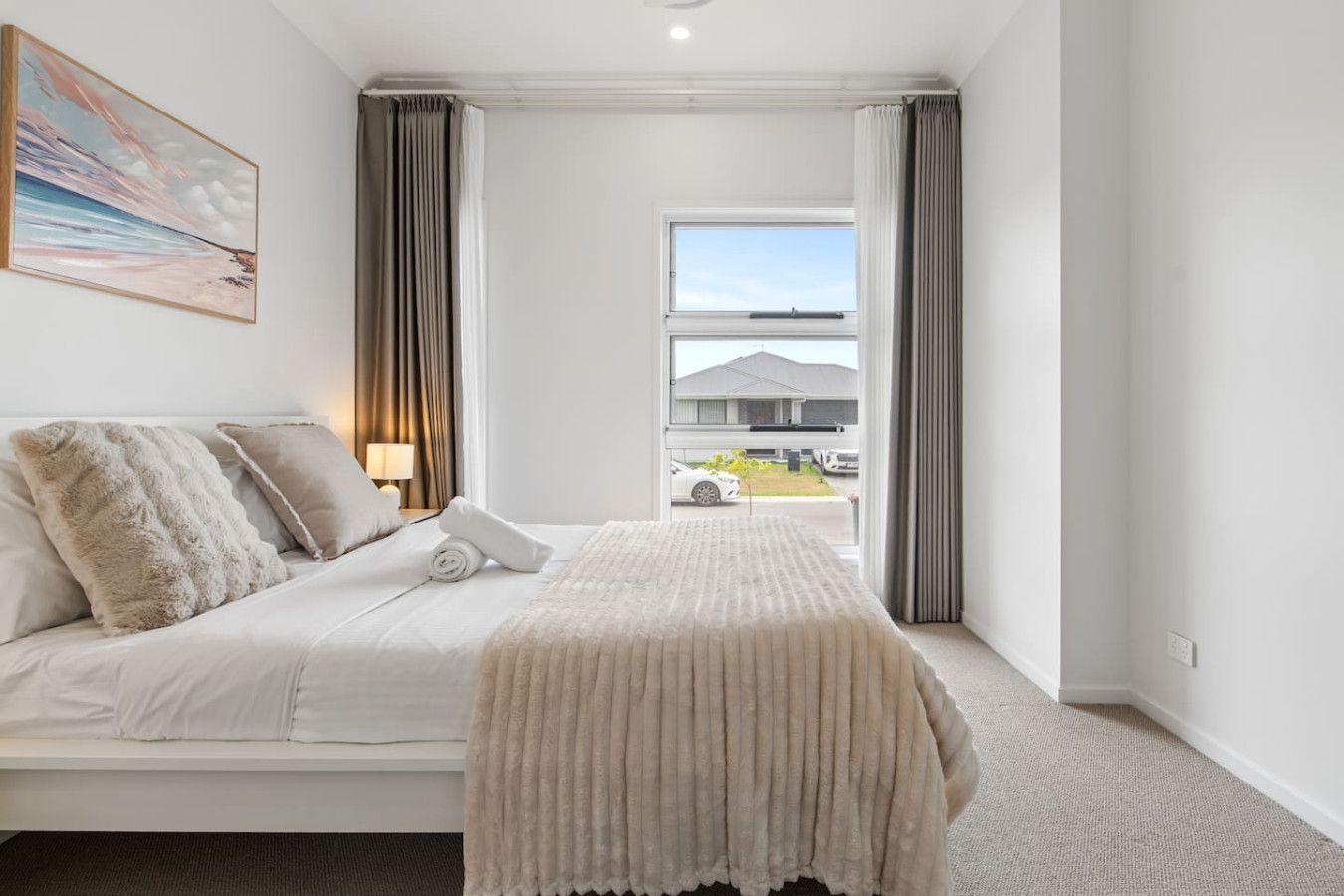 Habitación de hotel con cama, ventana con cortinas, un cuadro en la pared y vista al exterior.