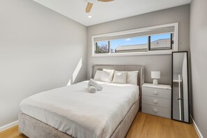 A bedroom with a bed, a nightstand, a mirror, and a window with a view of buildings. - Modern Family Oasis Luxe w/ Balcony A/C & Backyard (Holland Park)