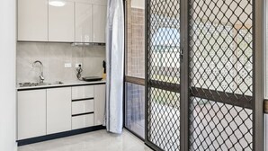 A modern kitchen with white cabinets, a stainless steel sink, and a window with a metal screen. - Cozy Little Charm Unit in Eight Miles Plain (Eight Mile Plains)