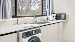 A compact kitchen with a washing machine, a coffee maker, and a microwave. - Cozy Little Charm Unit in Eight Miles Plain (Eight Mile Plains)