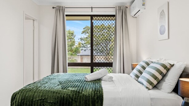 A bedroom with a bed, a nightstand, a lamp, a window with curtains, and a view of the outside. - Cozy Little Charm Unit in Eight Miles Plain (Eight Mile Plains)