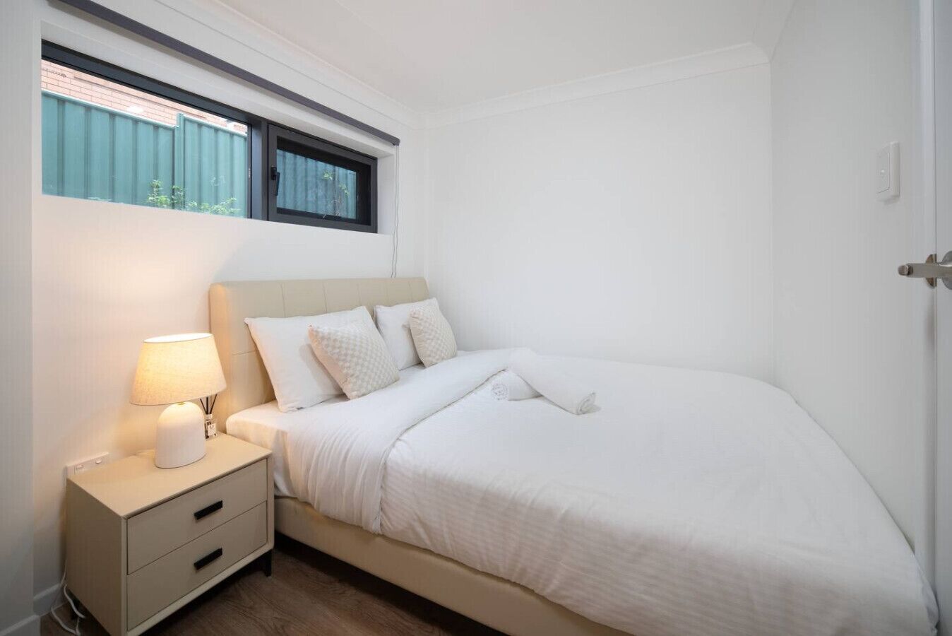 A neatly made bed with a headboard, a bedside lamp, and a nightstand with drawers.