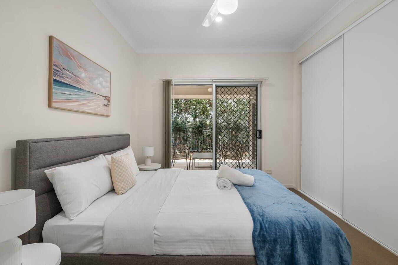 A bedroom with a bed, bedside table, lamp, and a view of an outdoor area through a sliding door.