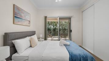 A bedroom with a bed, bedside table, lamp, and a view of an outdoor area through a sliding door.