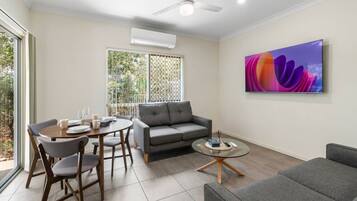 A modern living room with a grey sofa, a round coffee table, and a dining table with chairs.