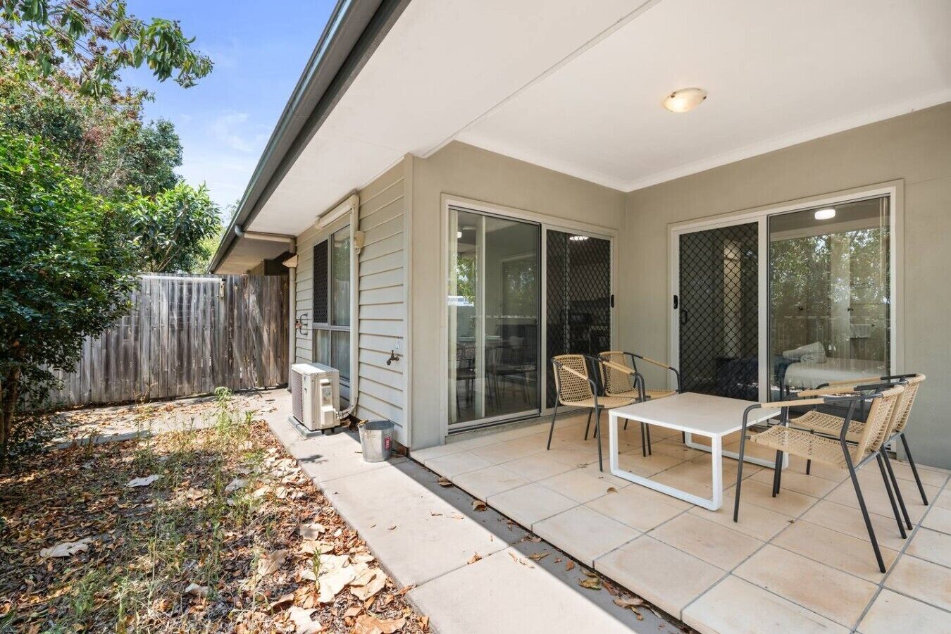 A patio with a table and chairs, a sliding glass door, and an air conditioning unit.