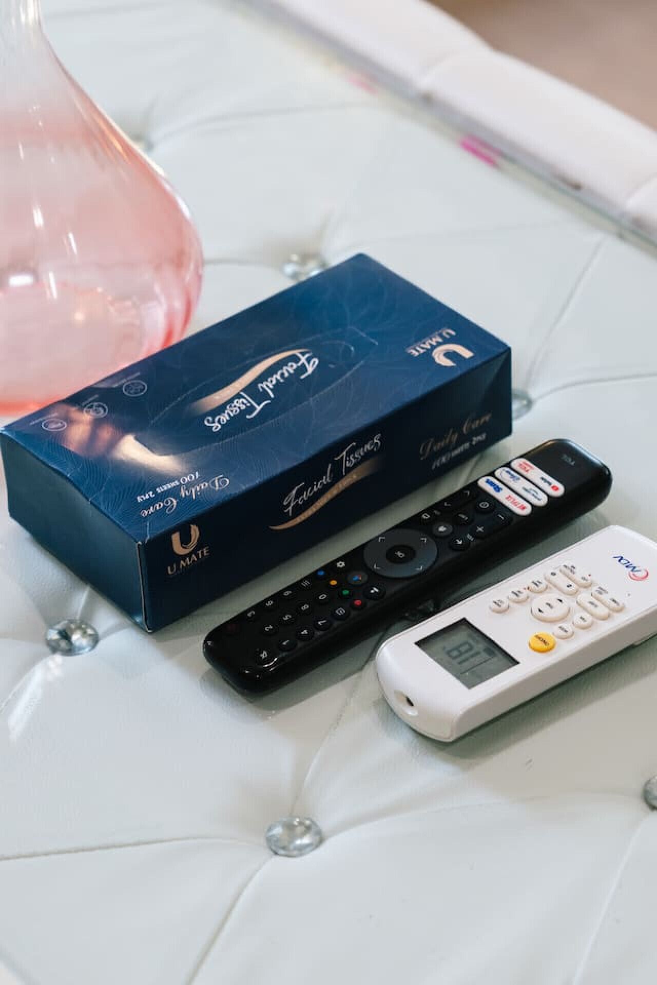 A box of U-Mate facial tissues and two remote controls on a white cushioned surface.