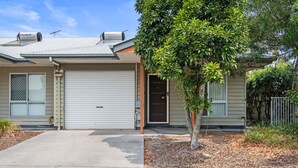 A single-story house with a garage door, a small tree in front, and a metal fence to the right.