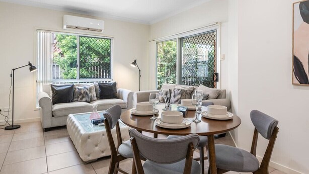 A modern living room with a dining area, featuring a sofa, a coffee table, and a dining table set for four.