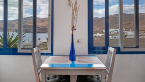 A dining table with a vase of dried plants, two chairs, and a view of a coastal landscape through large windows. - Unit 1 with Sea View, Shared Terrace and Wi-Fi (Yaiza)