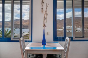 A dining table with a vase of dried plants, two chairs, and a view of a coastal landscape through large windows. - Unit 1 with Sea View, Shared Terrace and Wi-Fi (Yaiza)