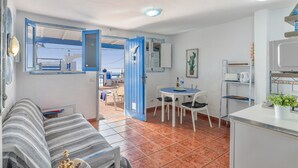 A compact living space with a sofa, dining table, chairs, a kitchen area, and a view through an open door.