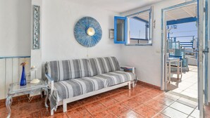 A room with a sofa, a table with a lamp, a decorative blue plate, and a window with a view.
