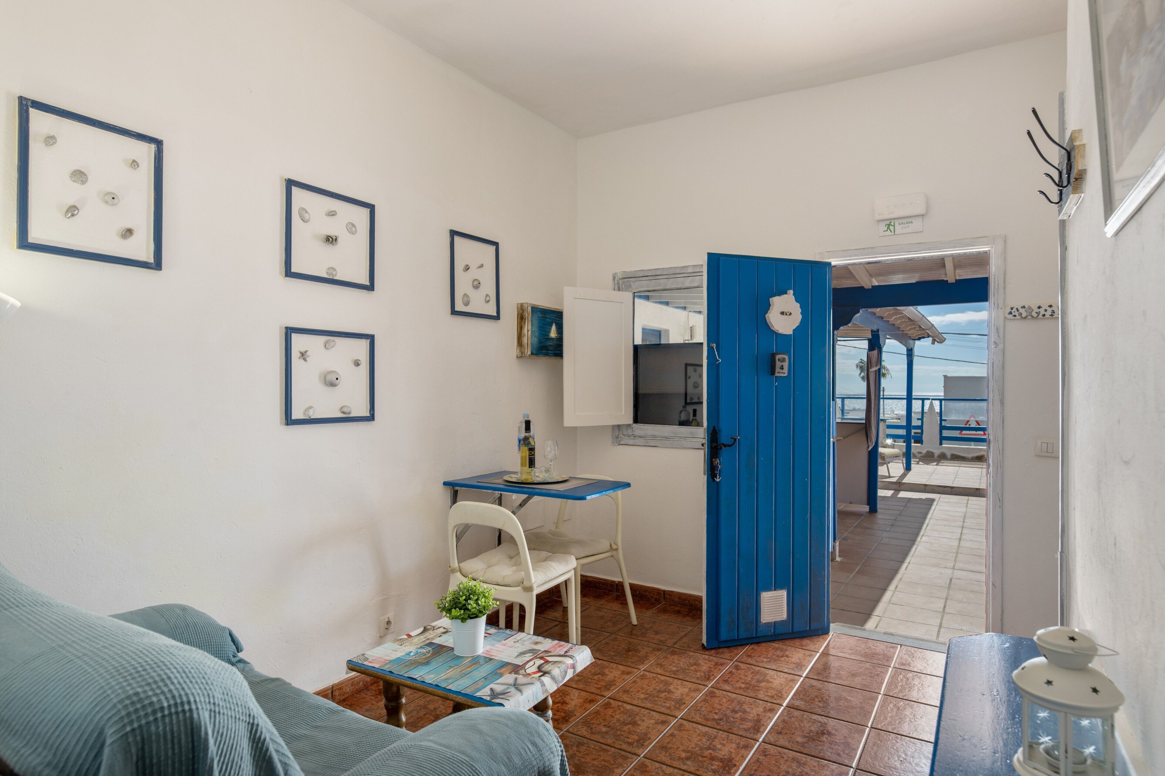 A room with a blue door, a small table with a chair, a sofa, and framed pictures on the wall.