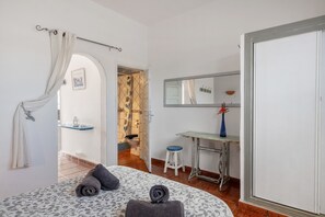 Een slaapkamer met een bed, bureau, spiegel en een badkamer die door een open deur zichtbaar is.