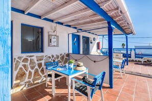 Een overdekt terras met blauwe stoelen en een tafel, een stenen muur en een blauwe deur.