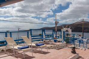 Een zonnig terras met lounge fauteuils, een stenen muur en uitzicht op zee en bergen.