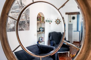 Ein Zimmer mit einem runden Spiegel, der einen Wohnbereich, ein Bücherregal, einen Garderobenständer und eine Tür zu einem anderen Raum reflektiert.