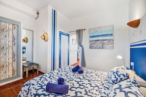 A bedroom with a patterned bedspread, a painting of a beach scene, and a view of the sea through a window. - Unit 5 'Ventanas de Lanzarote' with Shared Terrace and Wi-Fi (Yaiza)