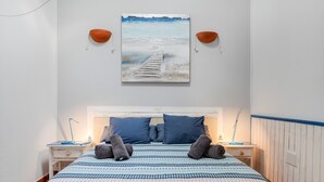 Een slaapkamer met een bed, hoofdeinde, twee nachtkastjes, een wandeling schilderij en een raam.