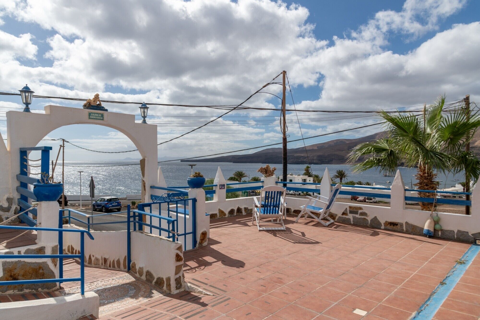 Une terrasse en bord de mer, dotée d’une balustrade bleue, d’une arche blanche et offrant une vue sur la mer.