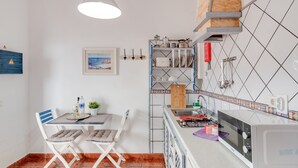Een kleine keuken met een magnetron, spoelbak en een eethoek met stoelen en een tafel.