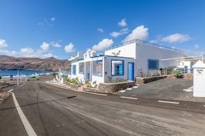 Una carretera costera con edificios blancos, una furgoneta verde y un cielo azul despejado.