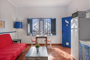 Une pièce avec un canapé rouge, une table entourée de chaises, une plante en pot, une porte bleue et un réfrigérateur.